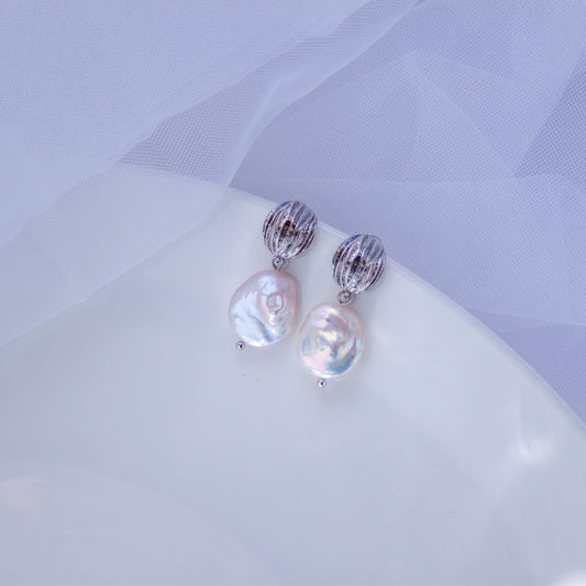 Pair of round flat baroque pearl drop earrings with silver textured tops on a soft white background