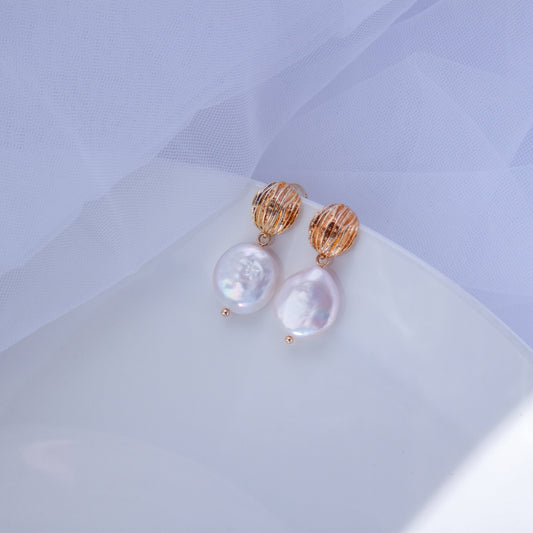 Gold drop earrings with coin-shaped baroque pearls on a light background.