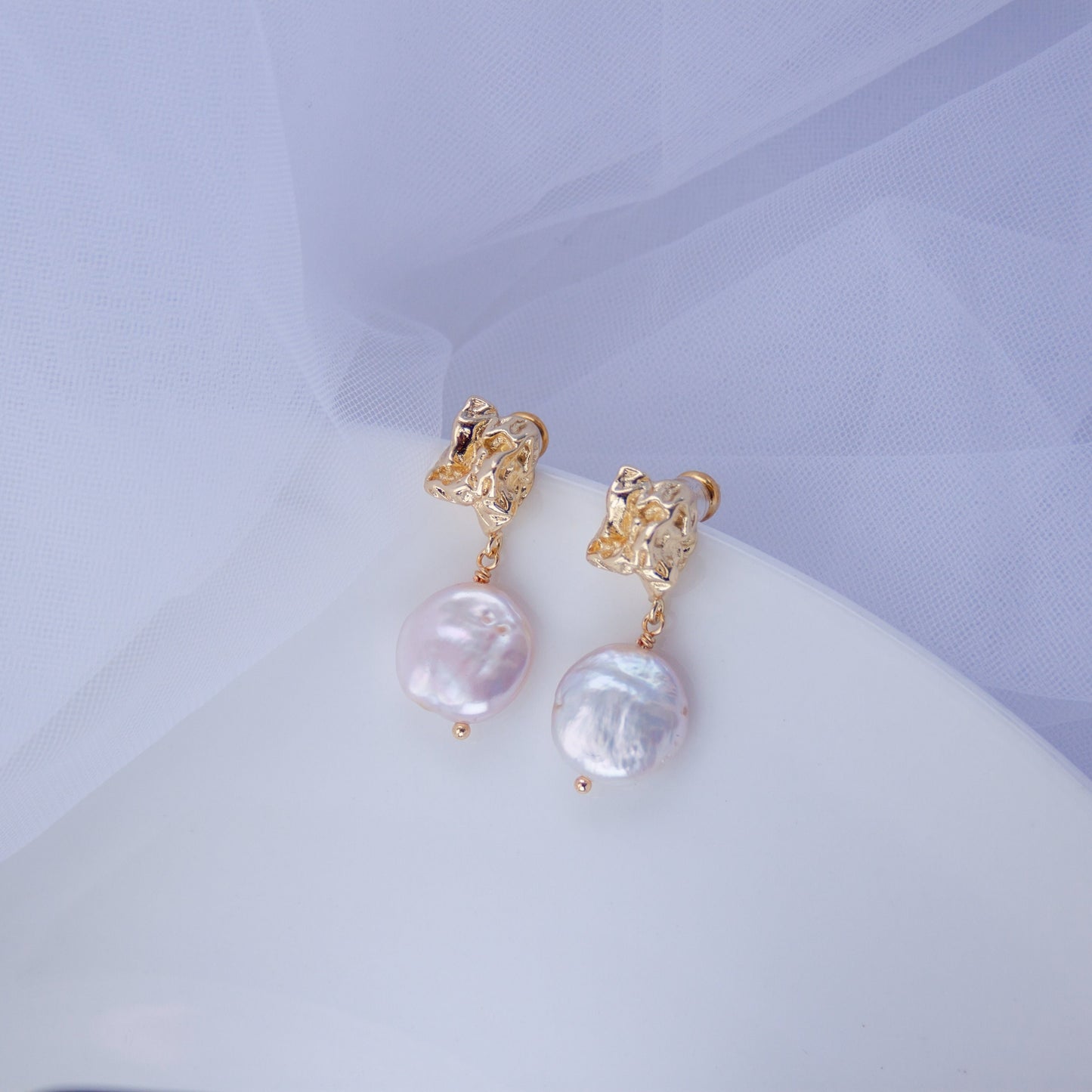 Pair of gold baroque drop earrings with irregular coin pearls on a soft white background