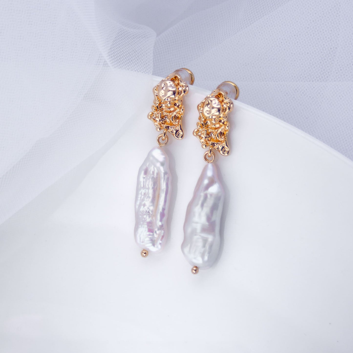 Baroque pearl drop earrings with irregular large freshwater pearls and gold-plated sculptural studs, bridal jewelry photographed on white plate with soft tulle fabric – Pearl Italy.