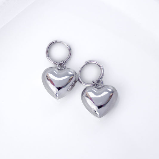 Pair of silver puffy heart hoop earrings on a white background