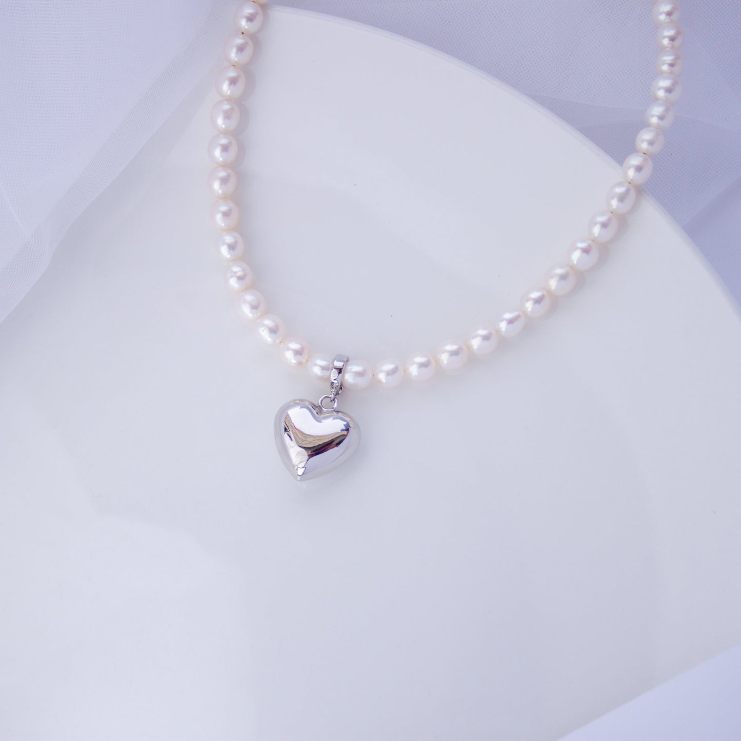 Freshwater pearl choker necklace with a silver heart pendant on a light background