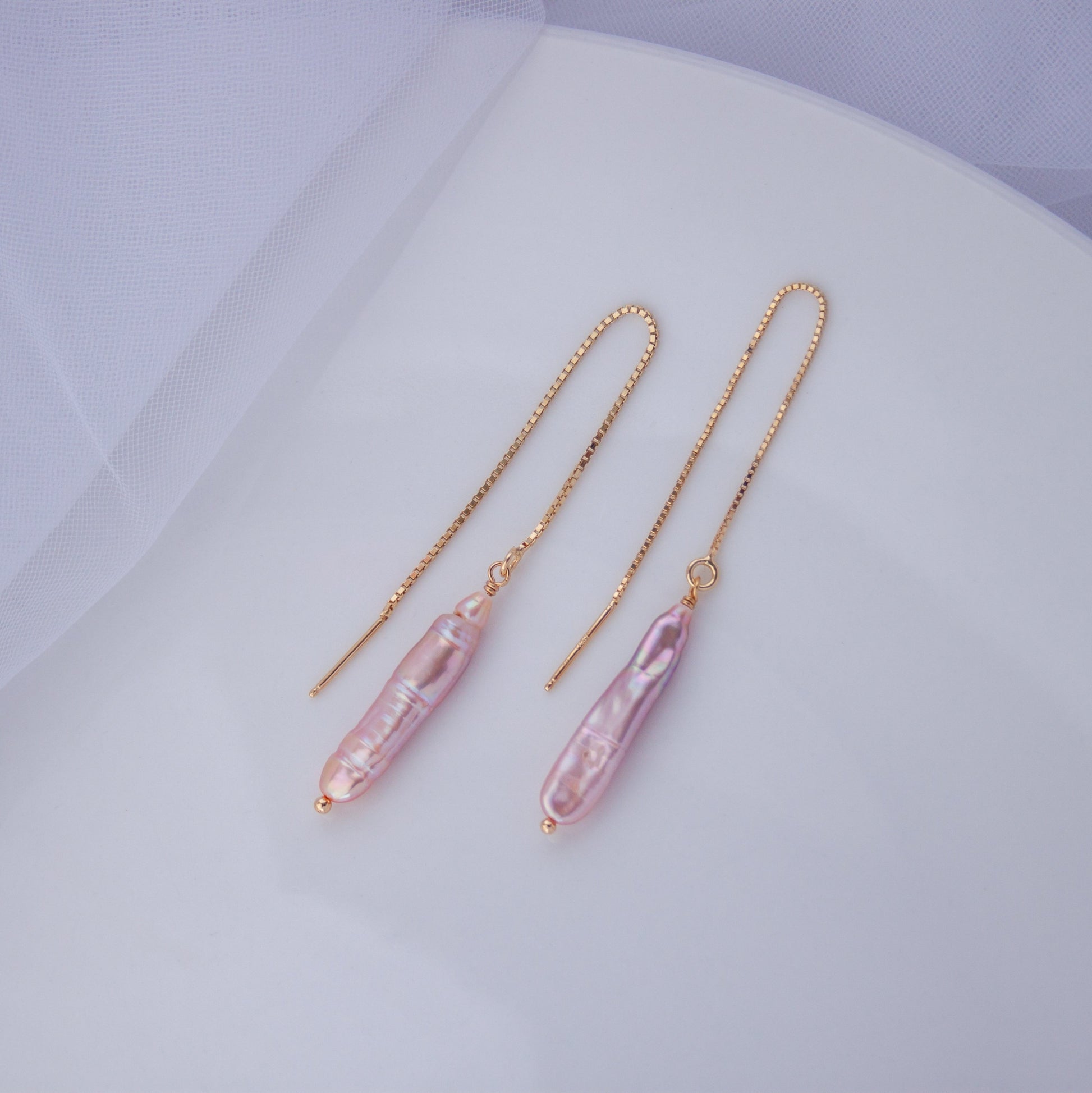 A pair of gold-plated silver chain earrings with pink baroque pearl threaders, displayed on a white surface.