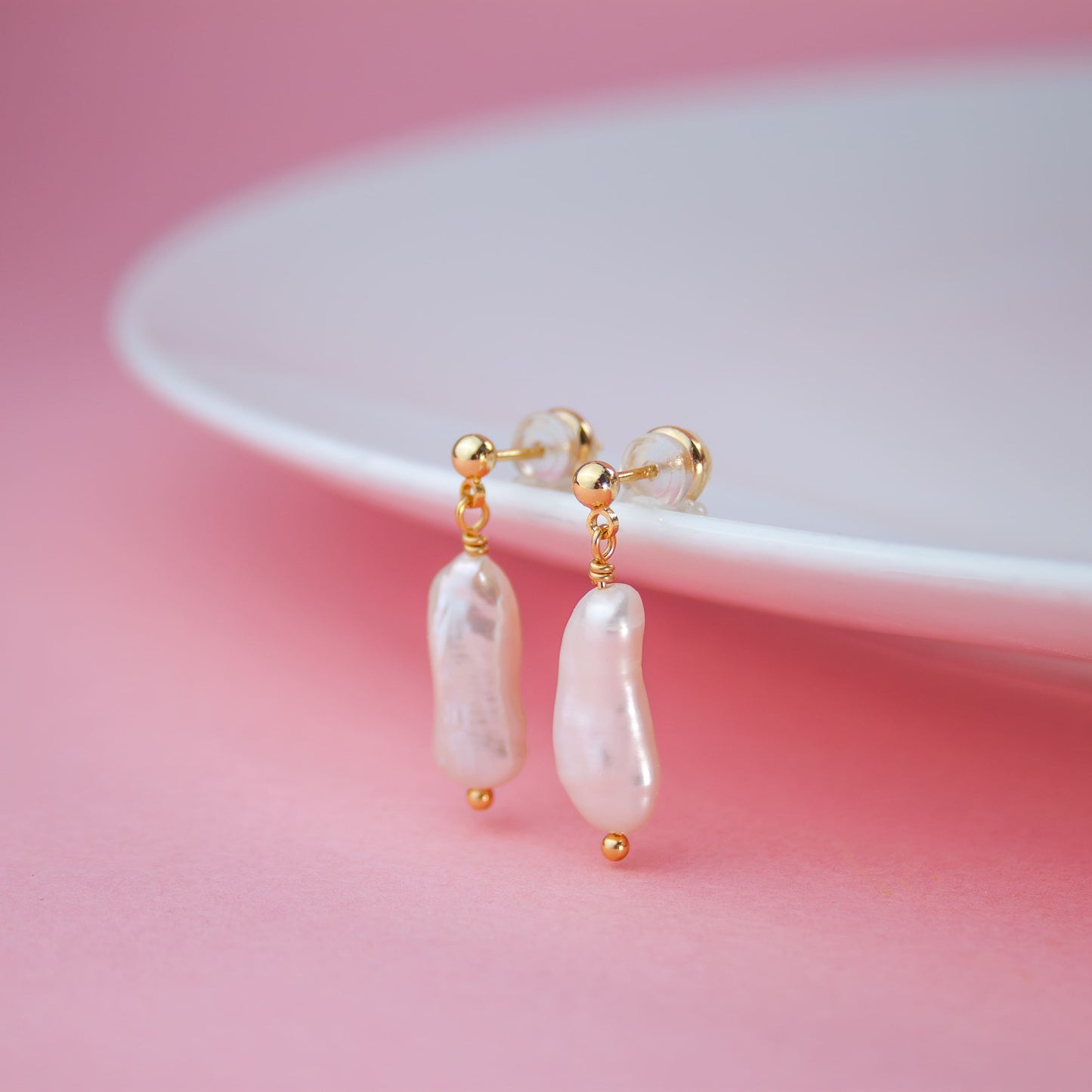 Pearl earrings with gold accents on a pink background