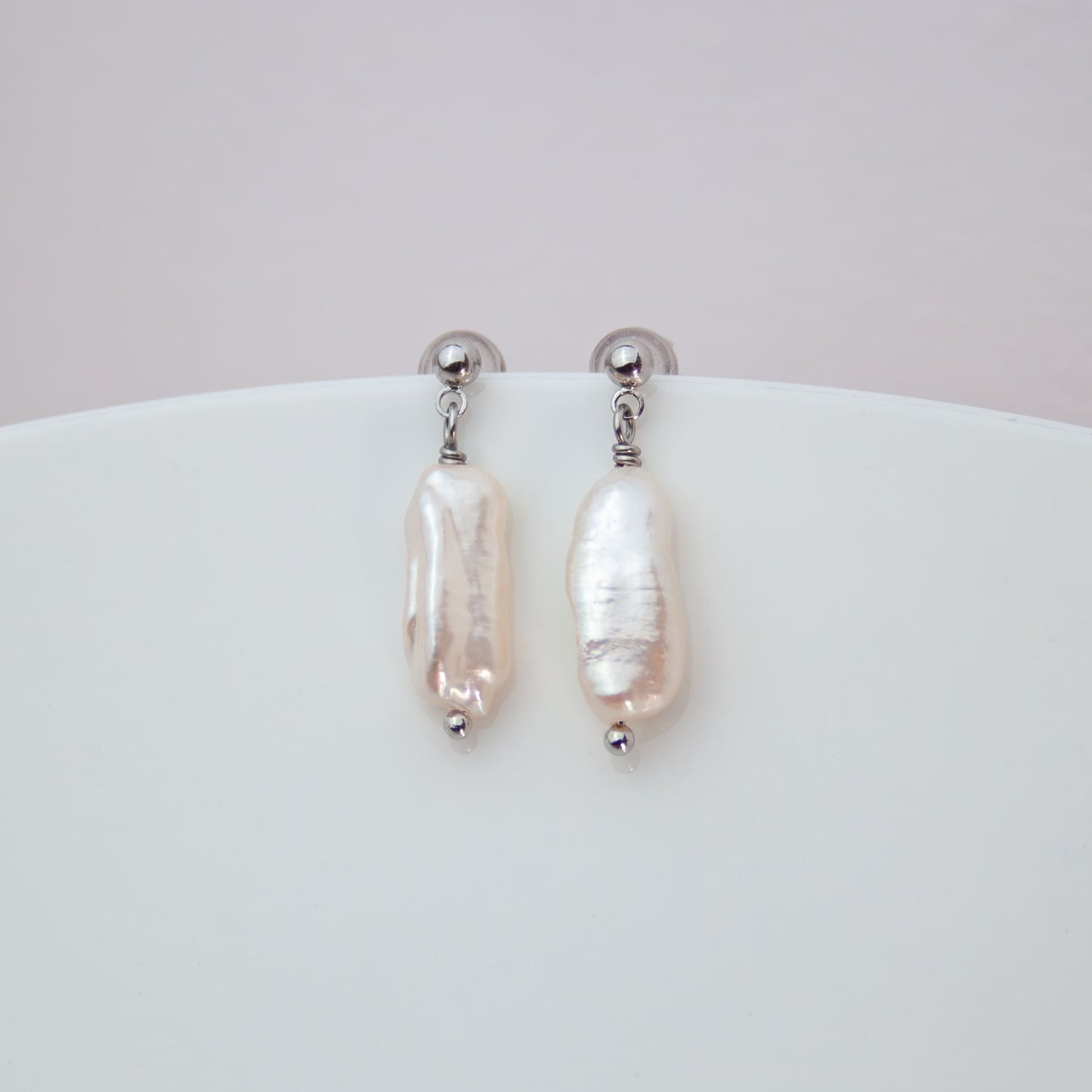Pearl earrings on a white surface with a light pink background
