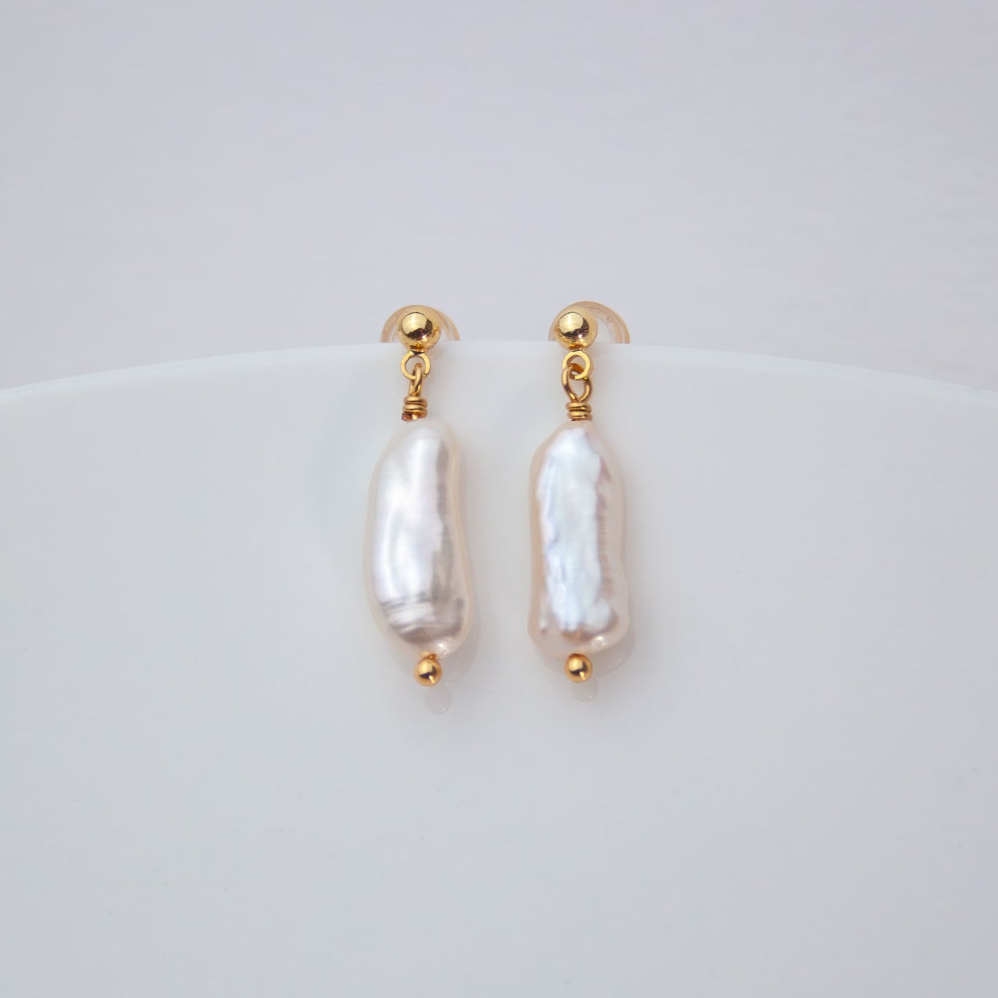 Pair of pearl earrings with gold accents on a light gray background