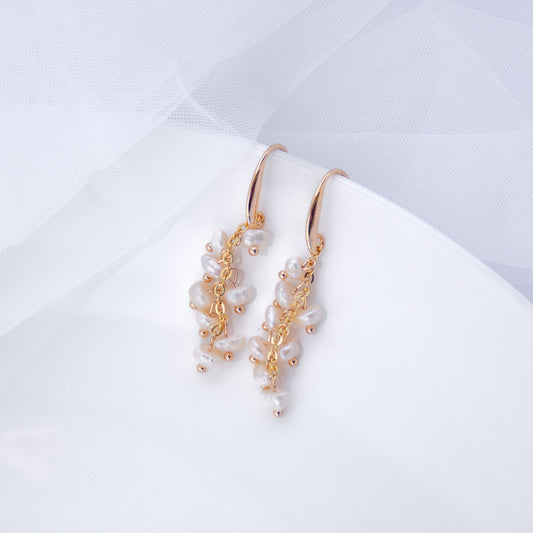 Gold hook earrings with small clusters of white freshwater pearls on a neutral background