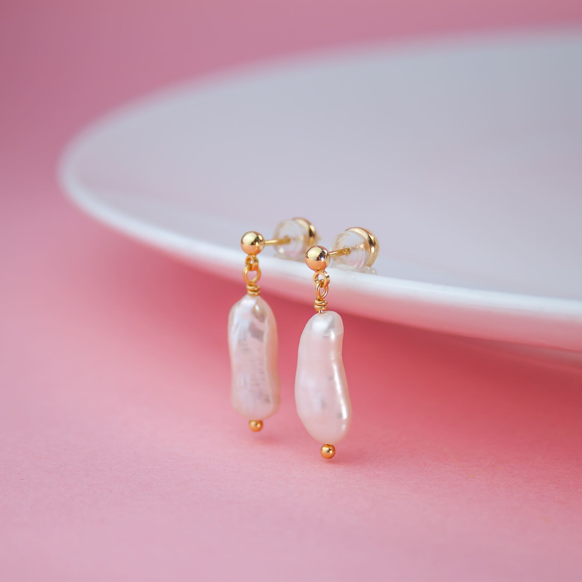 Pearl earrings with gold accents on a pink background