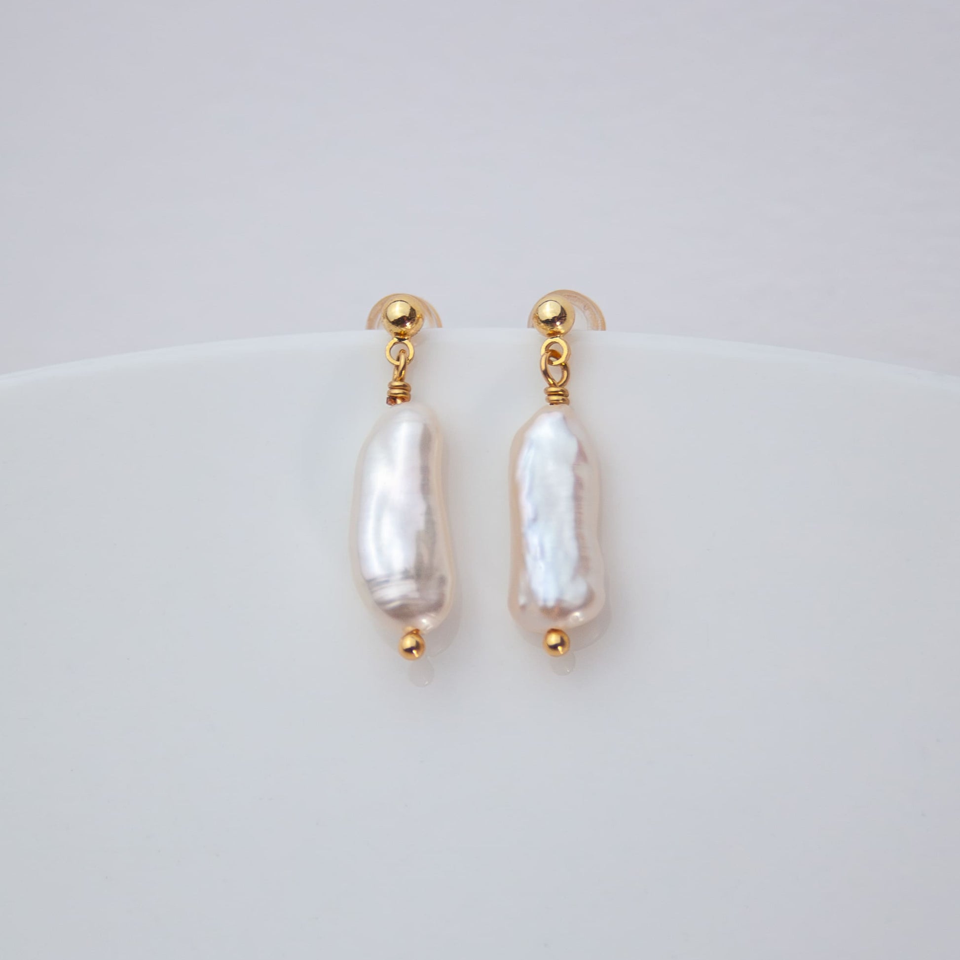 Pair of pearl earrings with gold accents on a light gray background