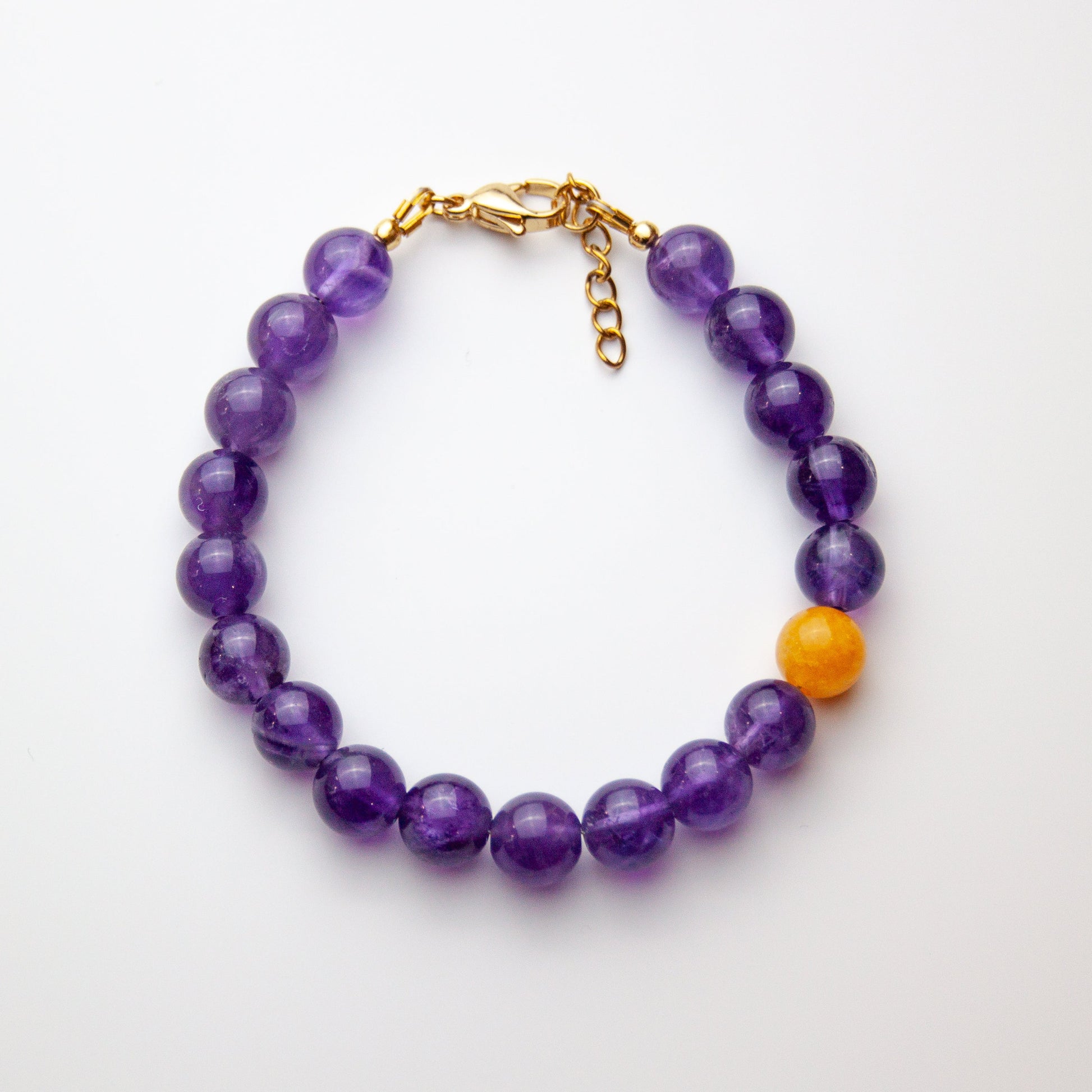 Amethyst bracelet with yellow agate accent and gold beads on white background