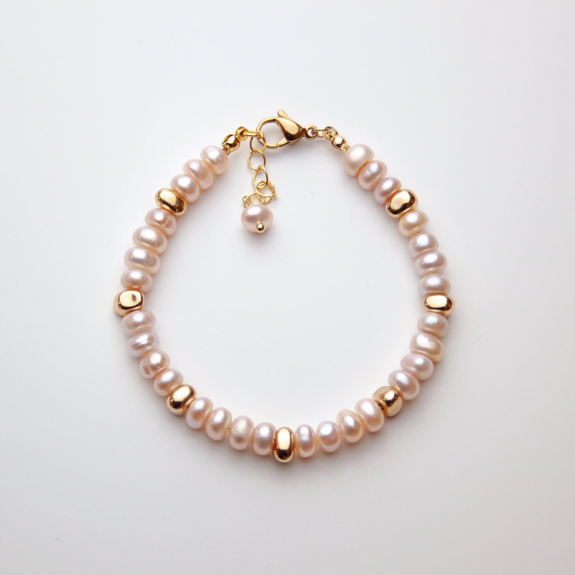 Pearl bracelet with gold clasp on a light gray background