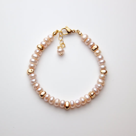 Pearl bracelet with gold clasp on a light gray background