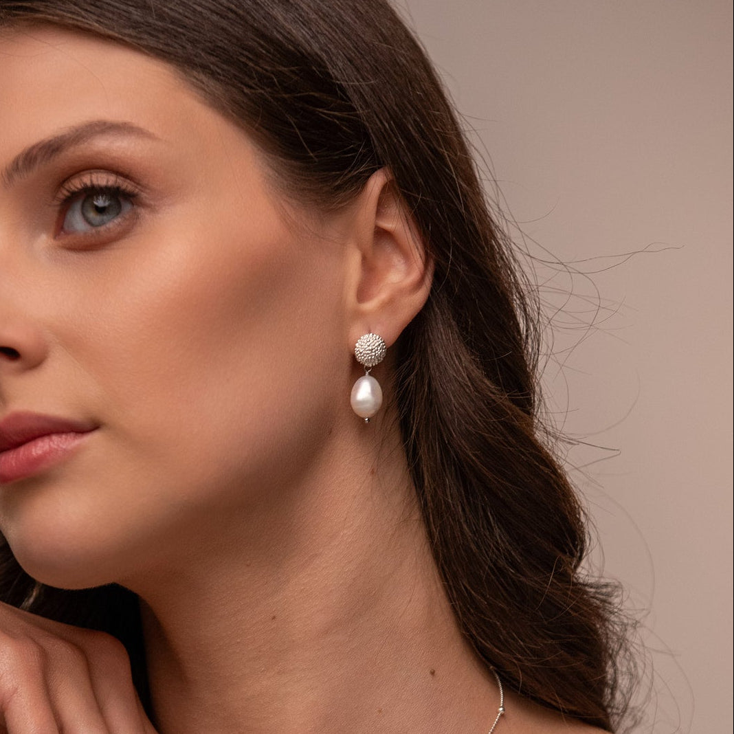 Close-up of a woman wearing pearl earrings with a neutral background